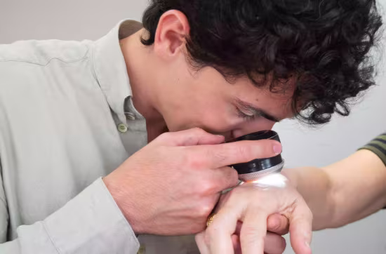 Dermatologista examina uma pinta com dermatoscópio durante uma avaliação da pele.