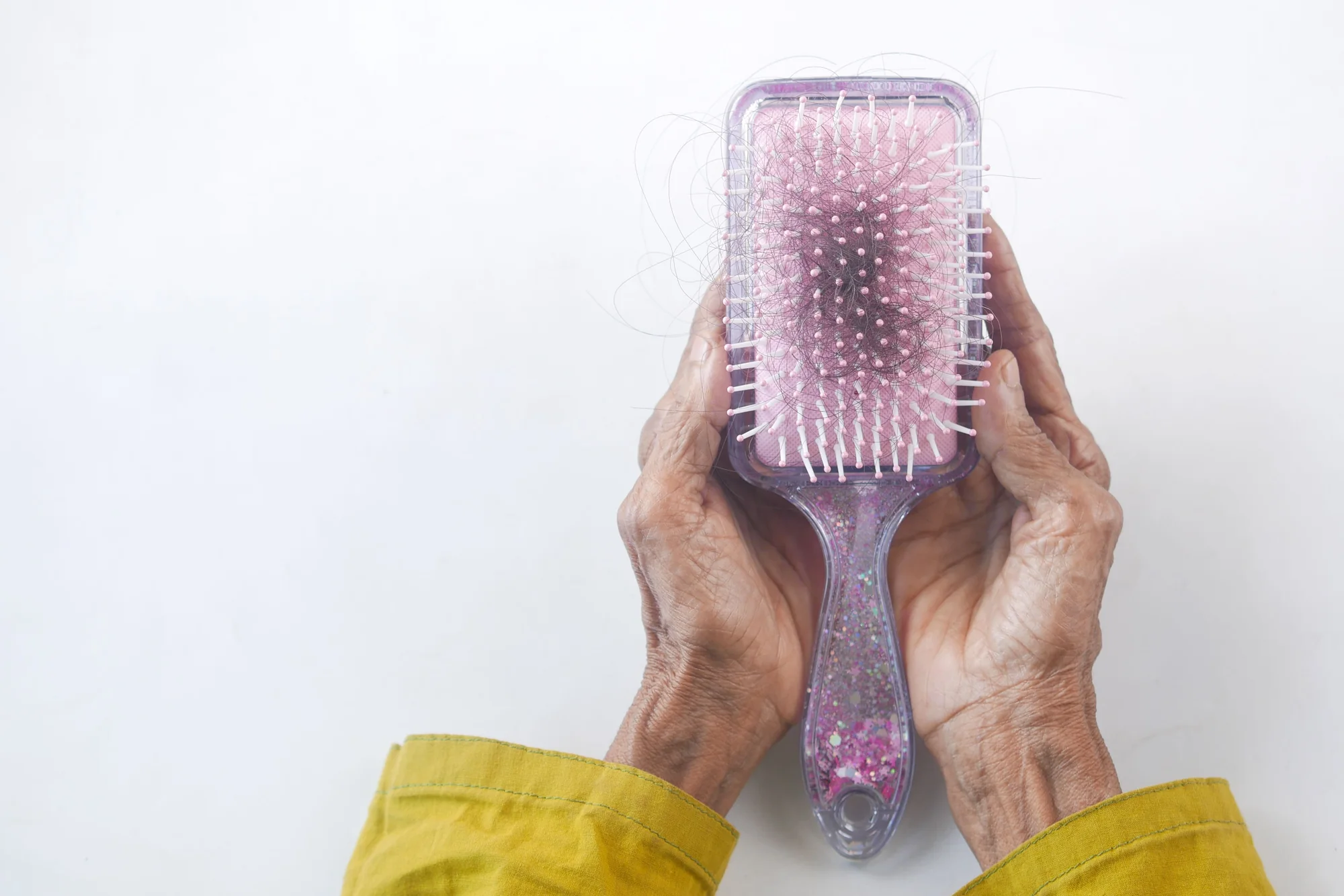 Mãos segurando fios de cabelo ao lado de uma escova, em fotografia ilustrativa.
