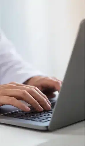 Mãos usando computador durante teleconsulta dermatológica; cena sintética ilustrativa, sem rostos ou dados reais.