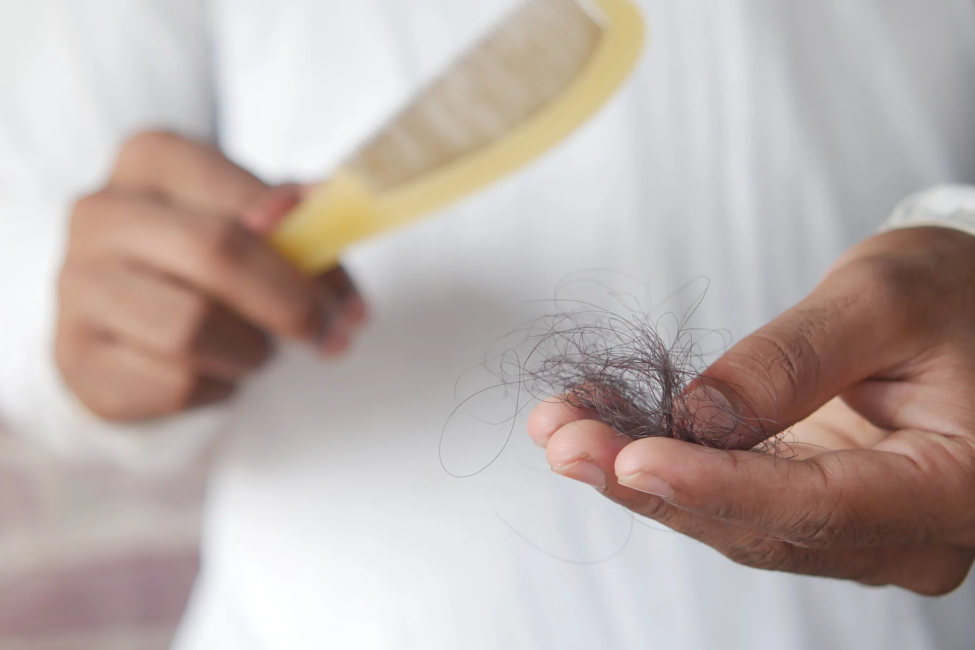 Pessoa observando fios de cabelo na mão ao lado de uma escova, em fotografia ilustrativa.