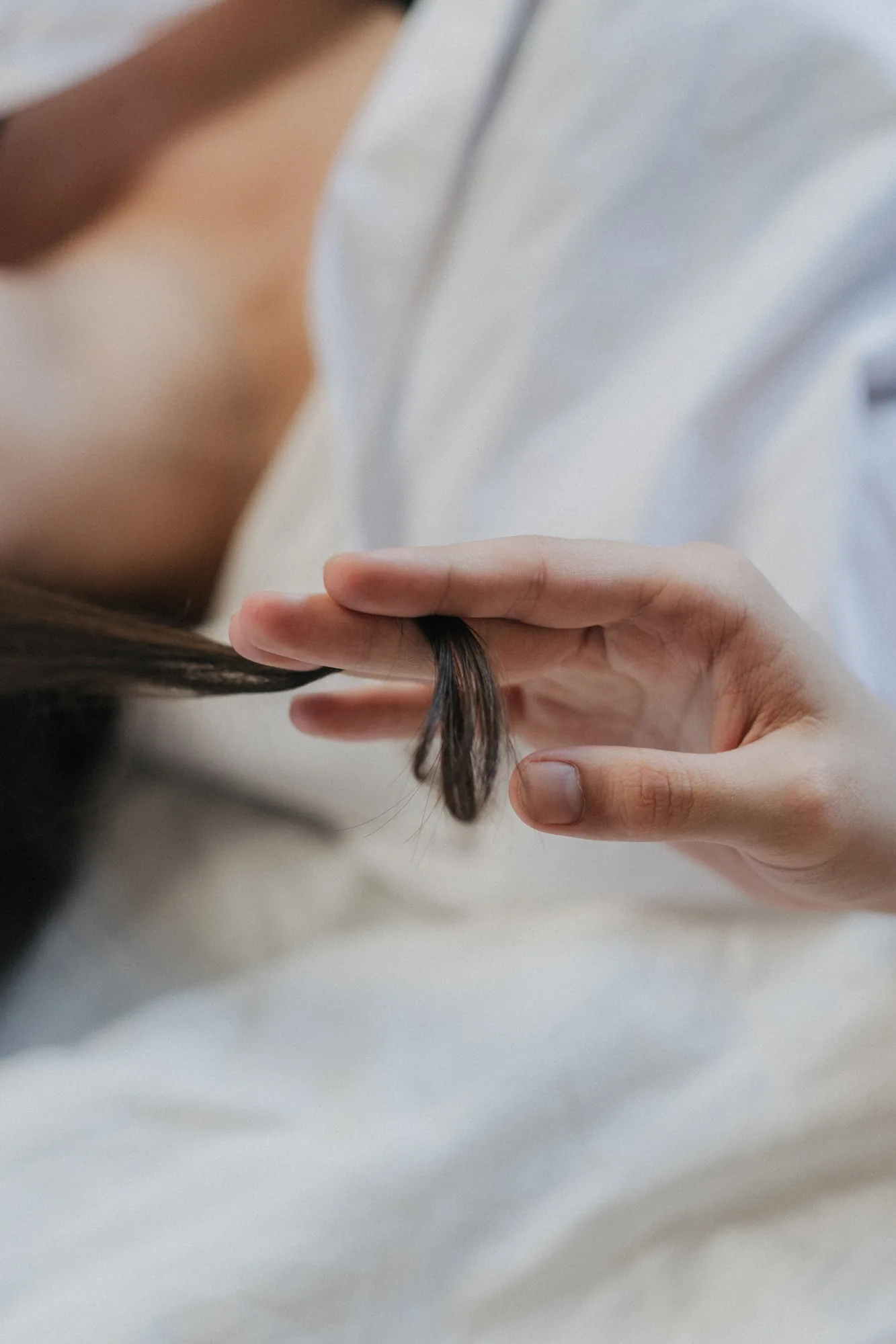 Mão segurando uma mecha de cabelo escuro, em fotografia ilustrativa.