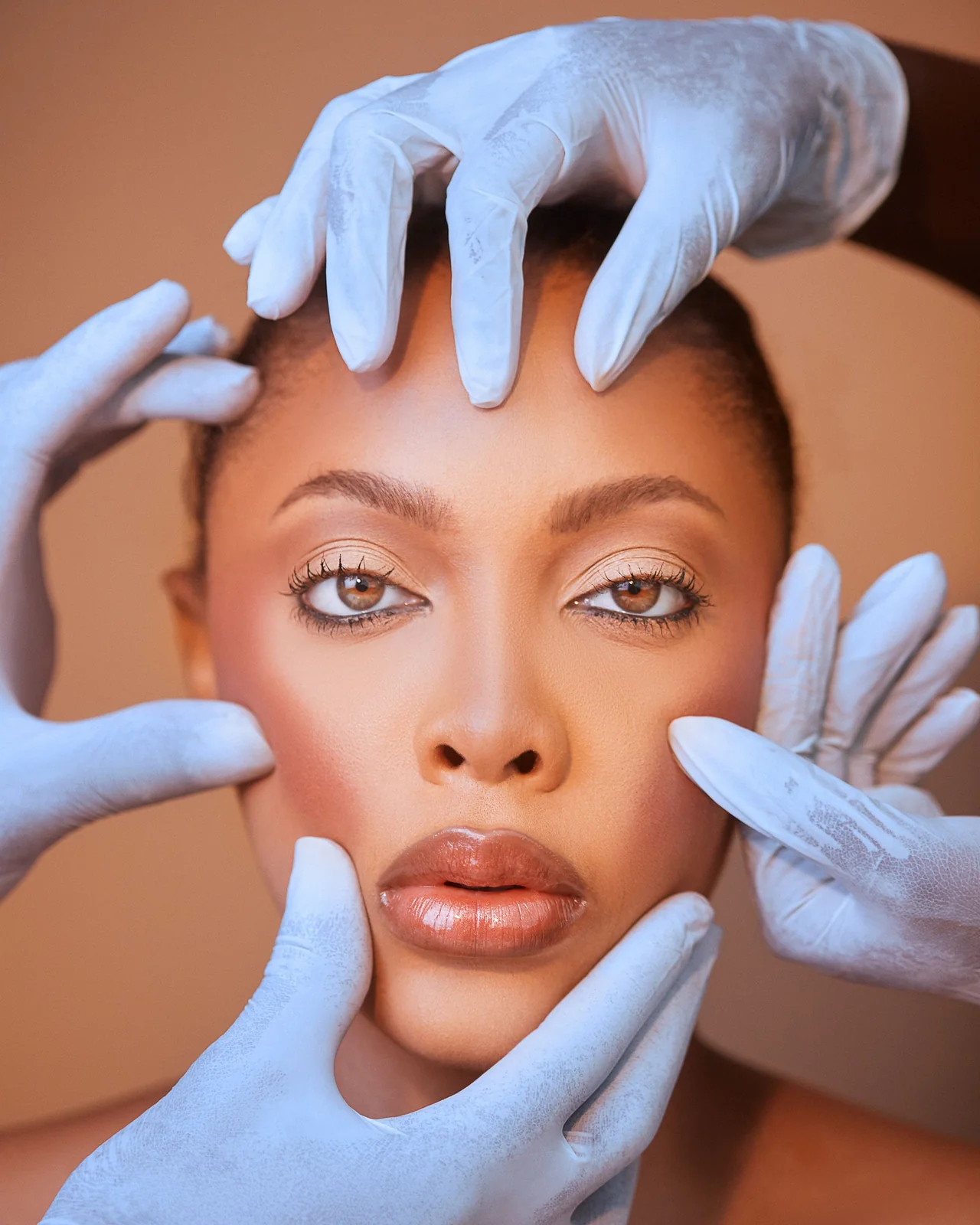 Mãos enluvadas apoiam o rosto de uma mulher durante uma avaliação facial ilustrativa.