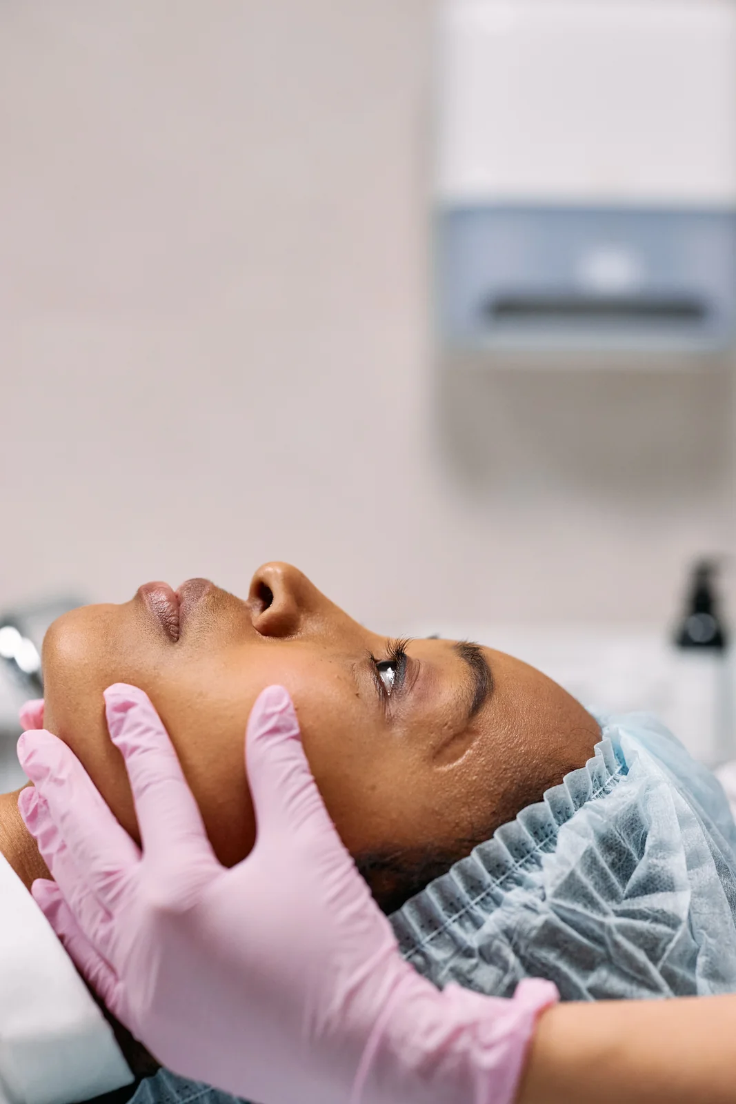 Pessoa deitada durante exame facial, com luvas clínicas apoiando o rosto.